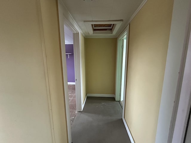 hall with concrete flooring, attic access, and baseboards