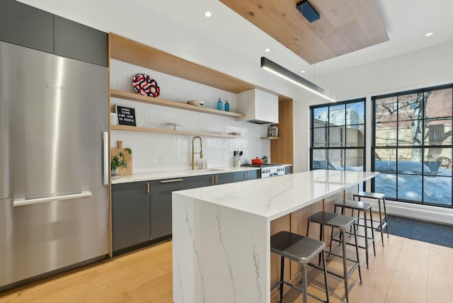 kitchen with light wood-style flooring, a sink, stainless steel refrigerator, open shelves, and a kitchen bar