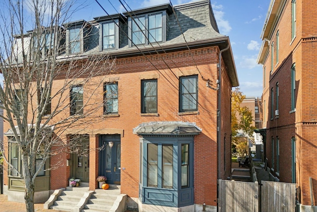 view of front of house featuring a shingled roof, entry steps, brick siding, and mansard roof