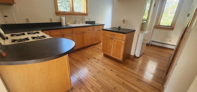 kitchen with a sink, light wood-style floors, baseboard heating, stovetop, and dark countertops