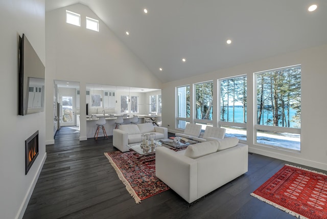 living area with dark wood-style flooring, recessed lighting, high vaulted ceiling, a warm lit fireplace, and baseboards