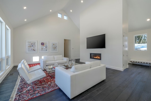 living area with high vaulted ceiling, a glass covered fireplace, dark wood-style flooring, and baseboards