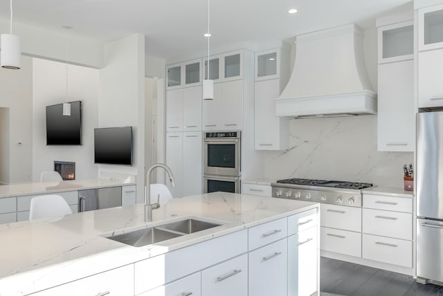 kitchen with decorative backsplash, custom range hood, appliances with stainless steel finishes, light stone countertops, and a sink