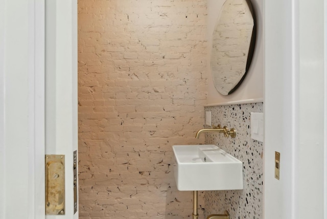 bathroom featuring brick wall and a sink