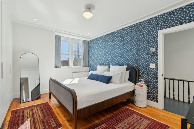 bedroom featuring baseboards, ornamental molding, hardwood / wood-style flooring, and wallpapered walls