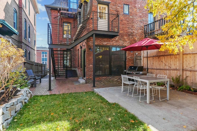 rear view of property featuring a patio, a balcony, brick siding, fence, and a yard