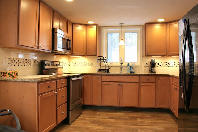 kitchen with decorative light fixtures, light wood-type flooring, decorative backsplash, stainless steel appliances, and a sink