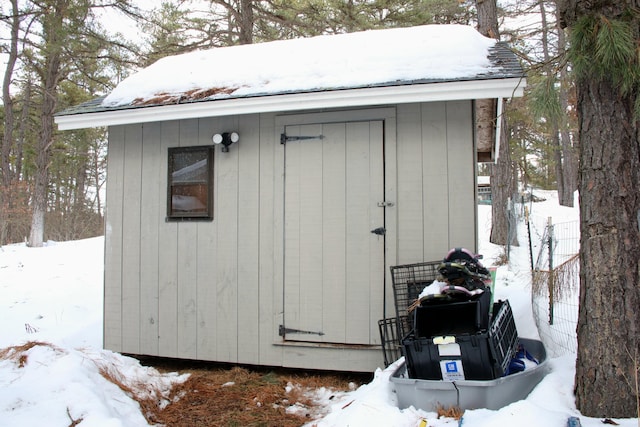 snow covered structure featuring an outbuilding and a shed