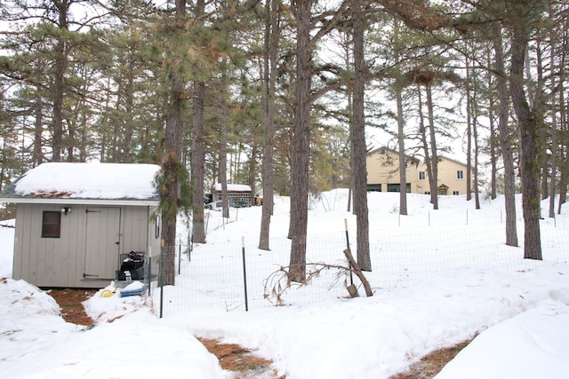 snowy yard featuring a storage shed, an outdoor structure, and fence