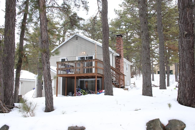 snow covered back of property featuring a chimney, a wooden deck, stairs, and a garage