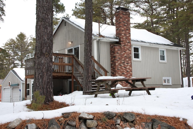 snow covered property with a garage, a deck, and a chimney