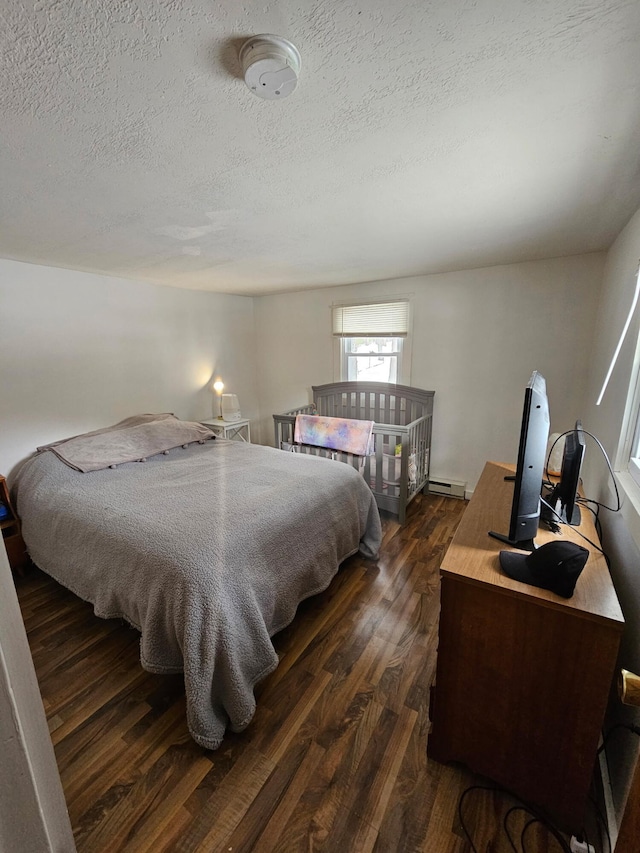 bedroom with dark wood-style flooring, baseboard heating, and a textured ceiling