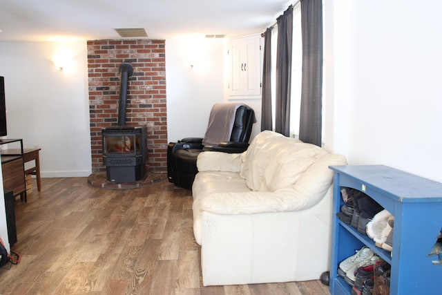 living area with visible vents, a wood stove, baseboards, and wood finished floors