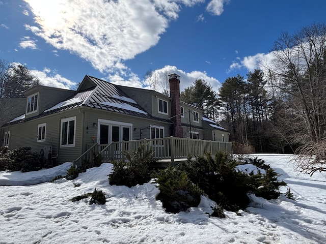 snow covered back of property with a chimney and a wooden deck