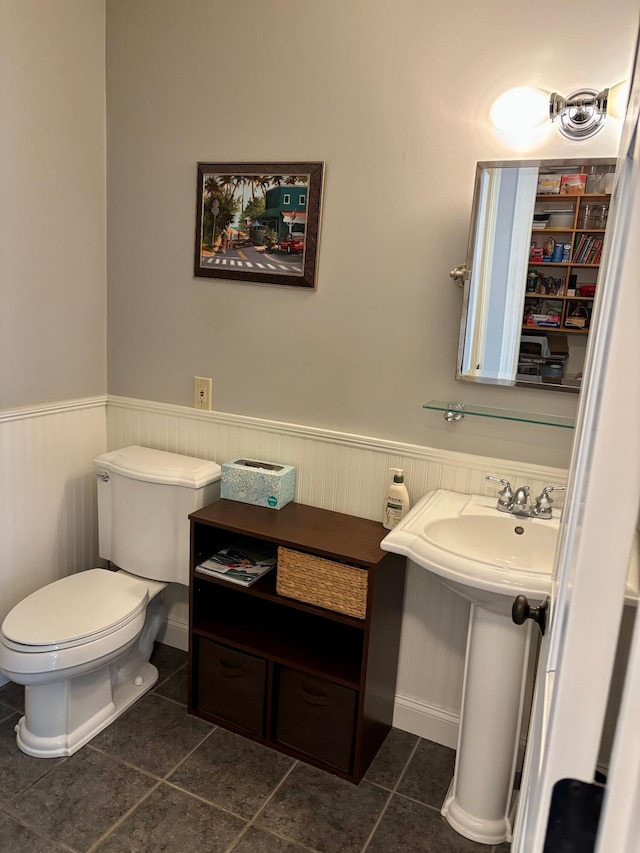 half bathroom featuring tile patterned floors, wainscoting, toilet, and a sink