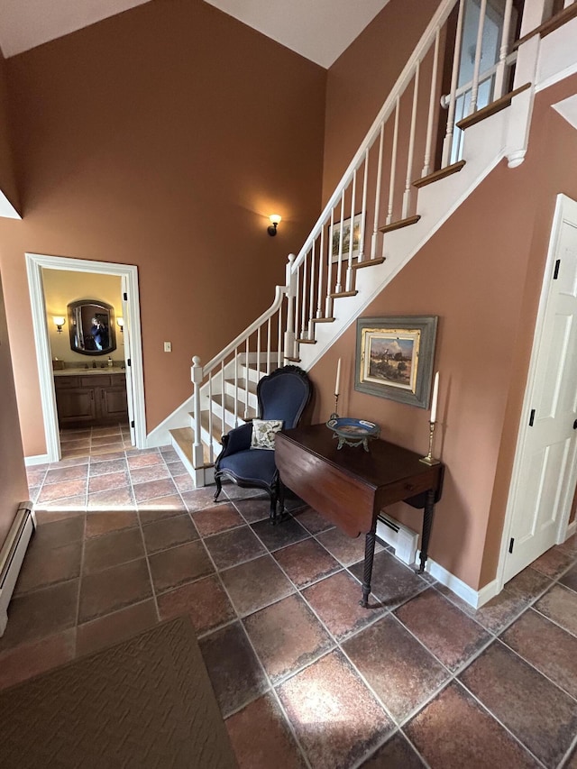 entrance foyer with stone tile floors, baseboards, stairs, a towering ceiling, and baseboard heating