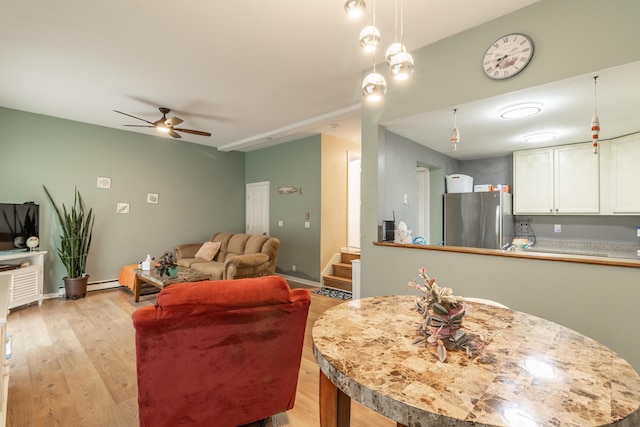 interior space featuring a baseboard heating unit, a ceiling fan, white cabinets, light wood-type flooring, and freestanding refrigerator