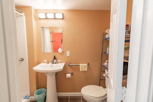 bathroom featuring toilet, a sink, tile patterned flooring, baseboards, and walk in shower