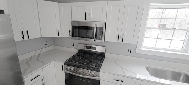 kitchen featuring a wealth of natural light, light stone countertops, appliances with stainless steel finishes, and white cabinets