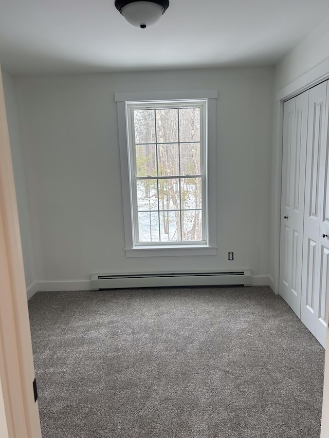 unfurnished bedroom featuring a baseboard heating unit, baseboards, a closet, and carpet flooring