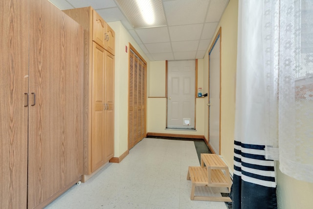 corridor with light floors, baseboards, and a paneled ceiling