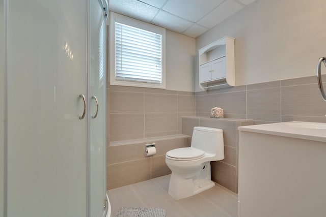 bathroom featuring a shower stall, a paneled ceiling, tile walls, toilet, and tile patterned floors