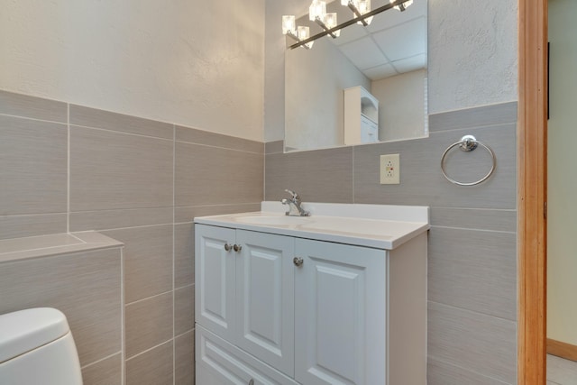 bathroom with tile walls, a drop ceiling, toilet, and vanity