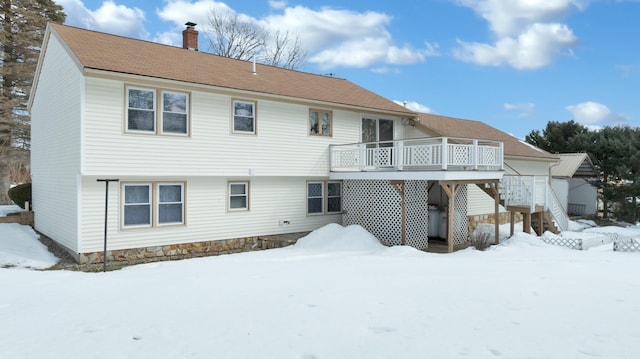 snow covered back of property with a deck, stairs, and a chimney