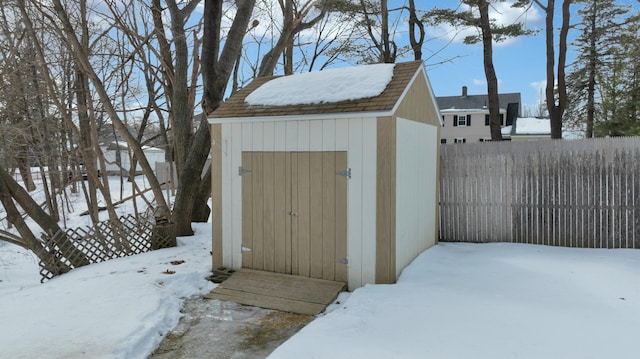 snow covered structure featuring an outdoor structure, a storage unit, and a fenced backyard