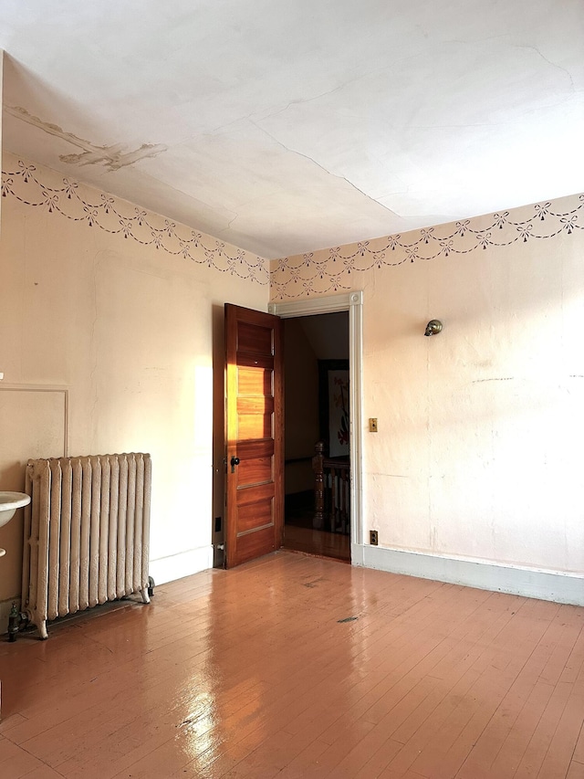 spare room featuring baseboards, wood finished floors, and radiator heating unit