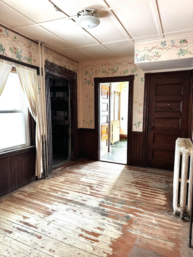 unfurnished room with wainscoting, wallpapered walls, radiator heating unit, and wood-type flooring