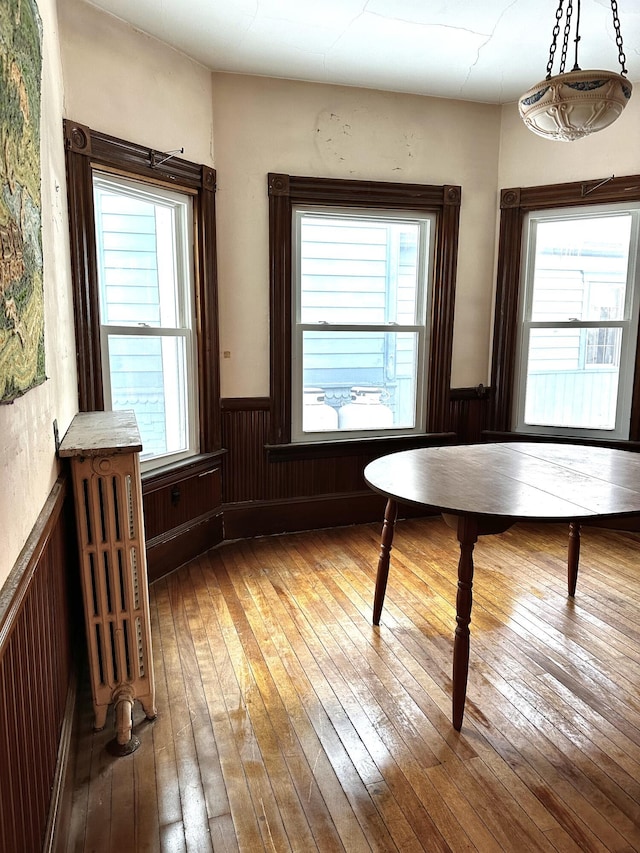 unfurnished dining area featuring a wainscoted wall, hardwood / wood-style floors, and radiator heating unit