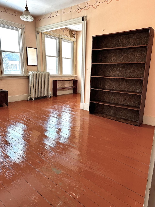 empty room featuring radiator heating unit, baseboards, and hardwood / wood-style flooring