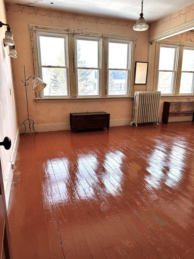 empty room featuring baseboards, radiator, a healthy amount of sunlight, and hardwood / wood-style floors