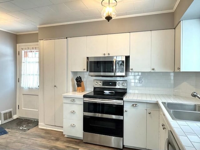 kitchen with visible vents, crown molding, tile counters, stainless steel appliances, and a sink