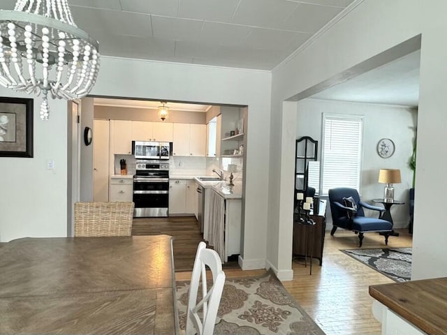 kitchen featuring ornamental molding, dark wood-type flooring, white cabinets, appliances with stainless steel finishes, and a notable chandelier