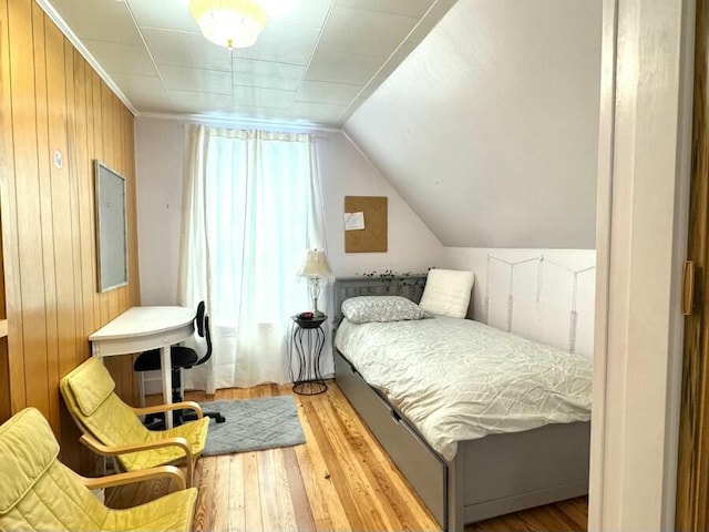 bedroom with vaulted ceiling, wooden walls, and hardwood / wood-style flooring