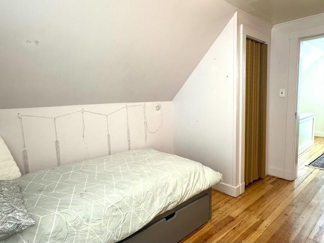 bedroom featuring baseboards, light wood-style floors, and vaulted ceiling