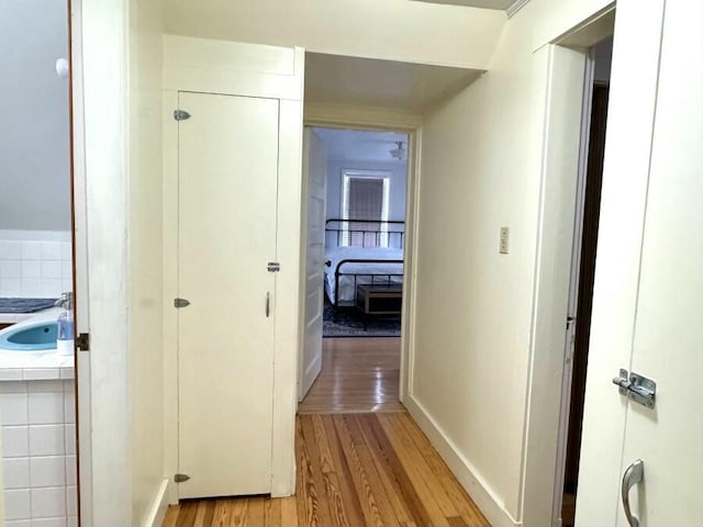 corridor with light wood finished floors, baseboards, and a sink