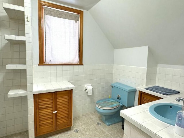 bathroom featuring tile patterned floors, toilet, a sink, tile walls, and lofted ceiling