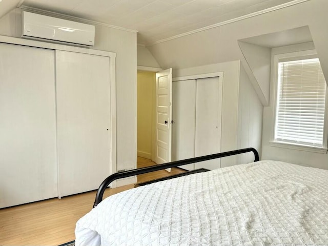 bedroom featuring a wall mounted air conditioner, multiple closets, ornamental molding, wood finished floors, and lofted ceiling