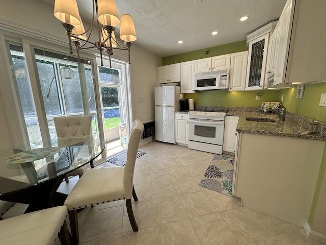 kitchen featuring glass insert cabinets, white cabinetry, a sink, dark stone counters, and white appliances