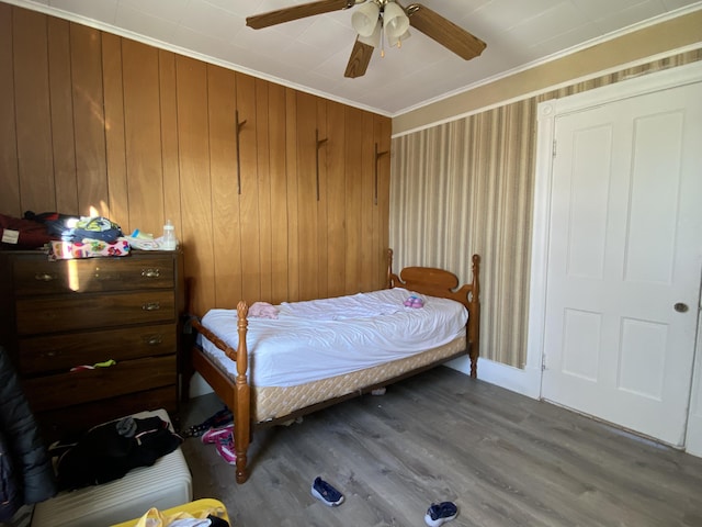 bedroom featuring ornamental molding, wood finished floors, a ceiling fan, and wooden walls