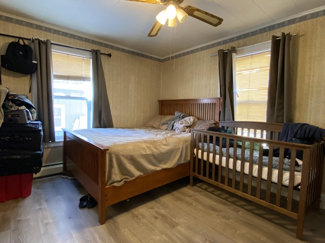 bedroom with a baseboard heating unit, wood finished floors, ornamental molding, and wallpapered walls