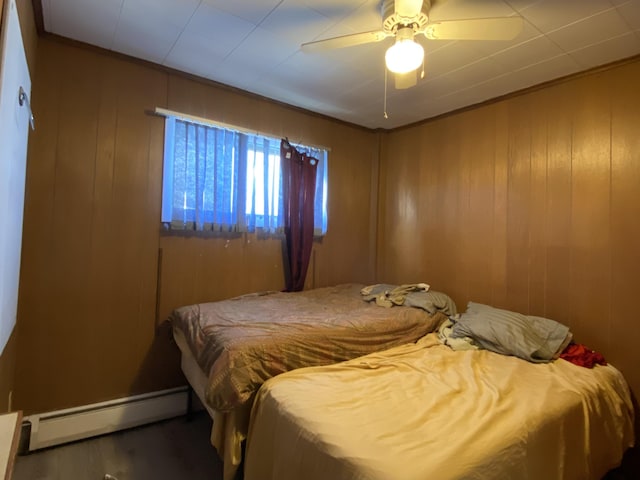 bedroom featuring crown molding, baseboard heating, wood walls, ceiling fan, and wood finished floors