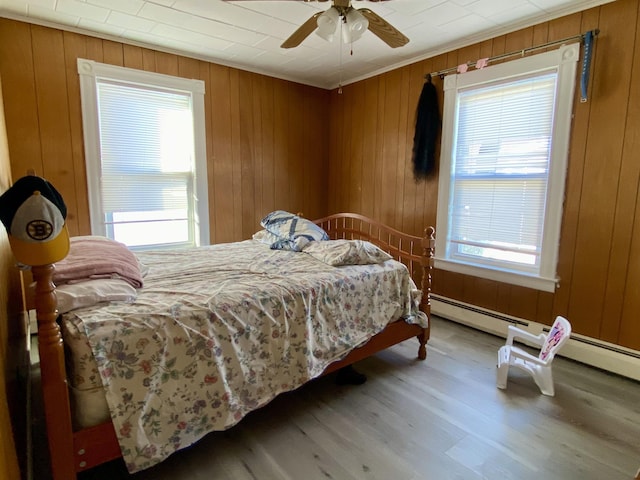 bedroom featuring a ceiling fan, multiple windows, wooden walls, and wood finished floors