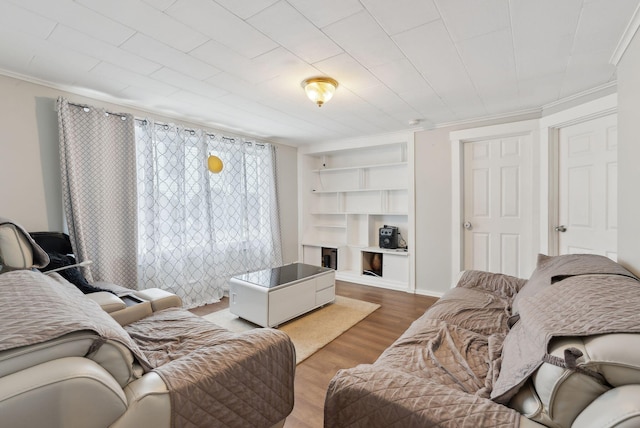 living area featuring built in features, ornamental molding, baseboards, and wood finished floors