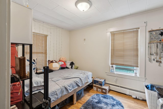 bedroom with crown molding, wood finished floors, and baseboard heating