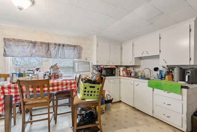 kitchen featuring ornamental molding, white cabinetry, light floors, and a sink