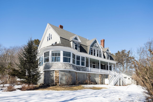 view of front facade with a porch, stone siding, stairway, roof with shingles, and a chimney